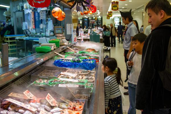 A family looks on as they shop for groceries. Seafood and fish are plentiful in every shop, very unusual compared to life in the US, even the PNW on the coast.